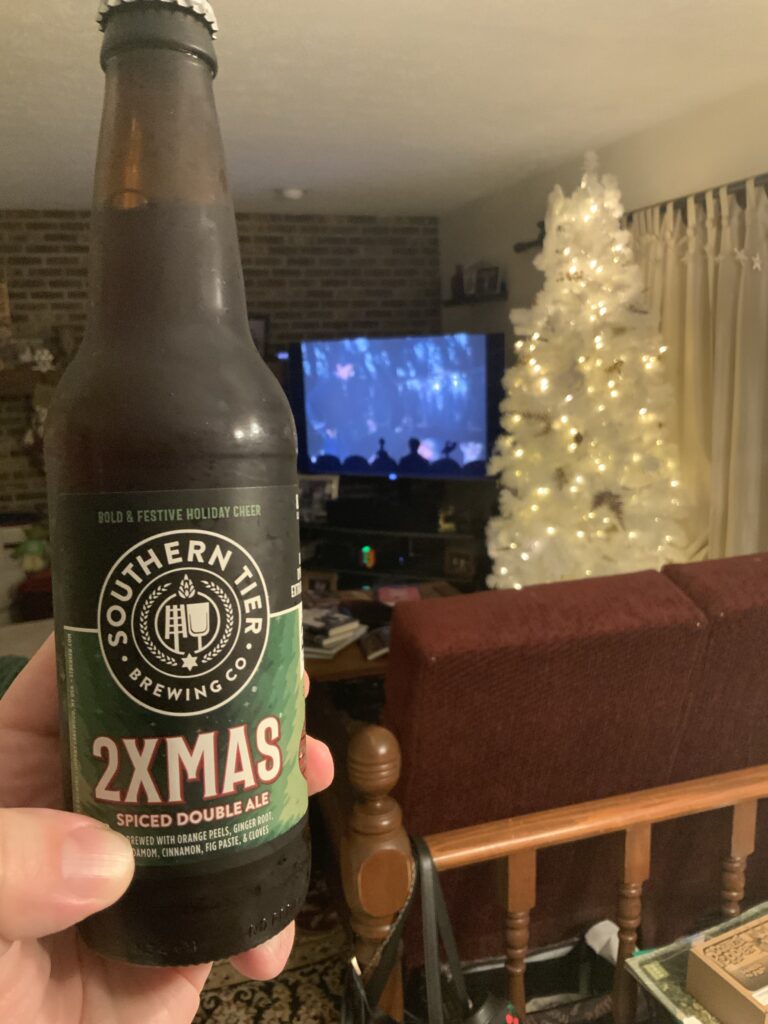 A bottle of Southern Tier 2XMas Spiced Double Ale with our Christmas tree and the MST3K riff of Cave Dwellers in the background