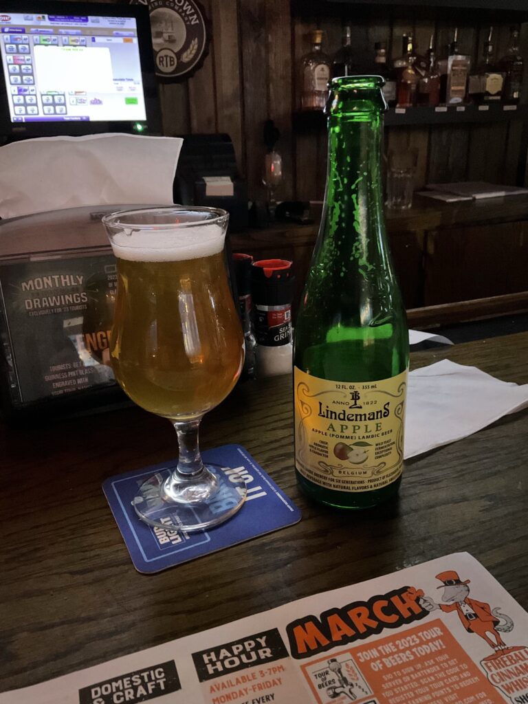 A glass of Lineman’s Pomme fruit lambic on the bar at the Winking Lizard. The bottle is to the right of the glass. 
