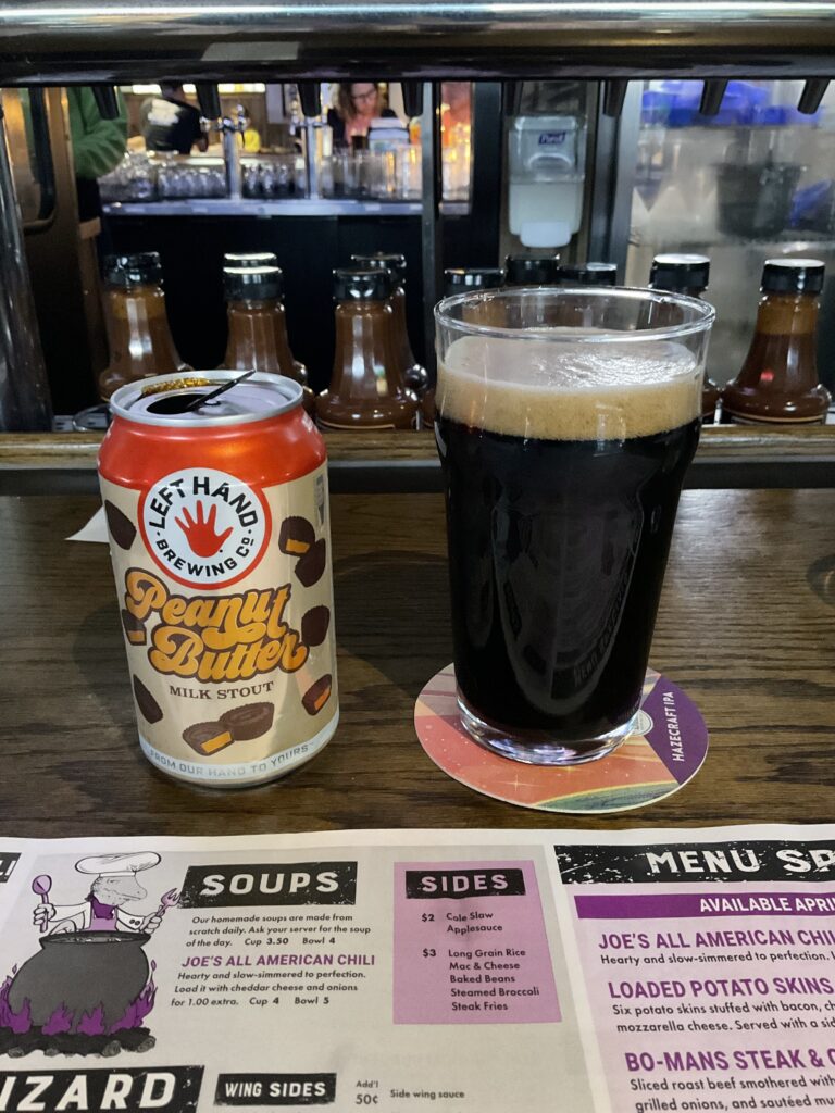 A glass of Left Hand Peanut Butter Milk Stout next to its can on the bar at the Winking Lizard