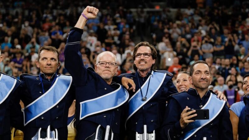 Members of the Bluecoats Alumni Corps drum line celebrating as the mass hornlines of the alumni and 2022 Bluecoats perform