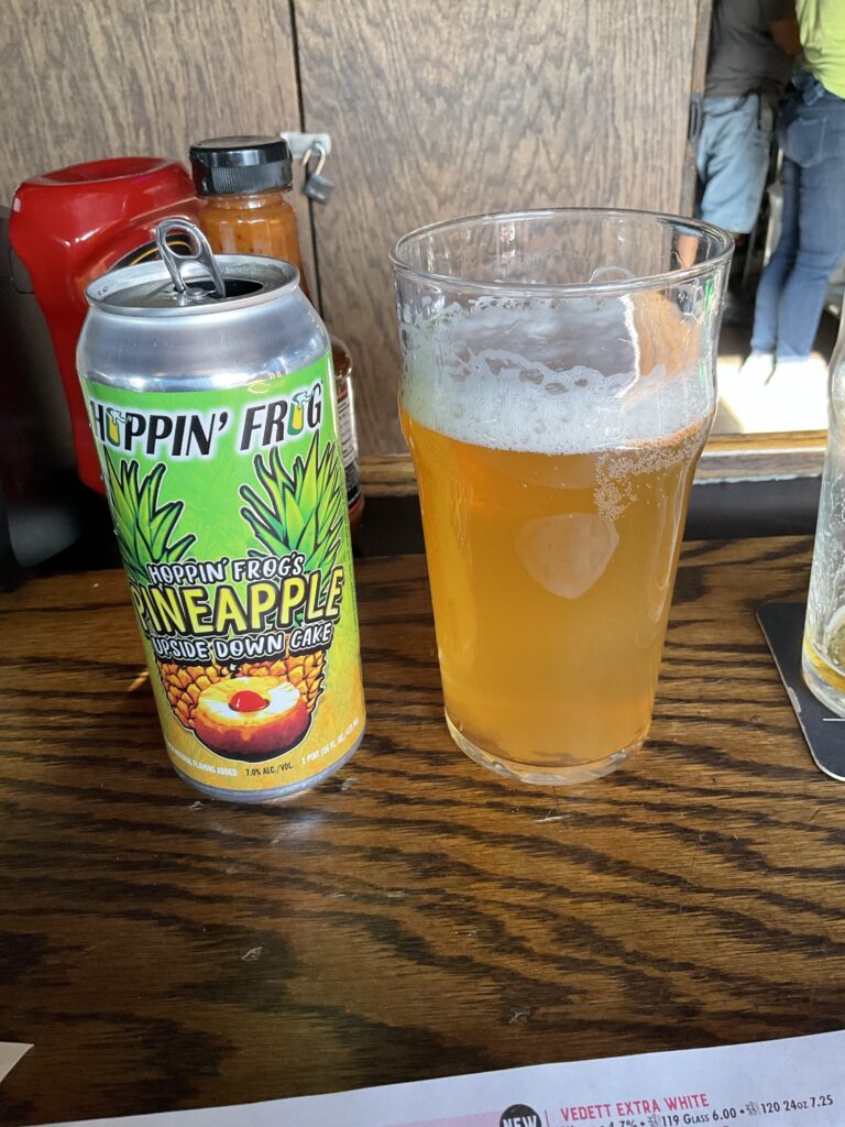 A glass of Hoppin’ Frog Pineapple Upside Down Cake fruit beer on the bar at the Winking Lizard. The beer’s can is to the left of the glass. 