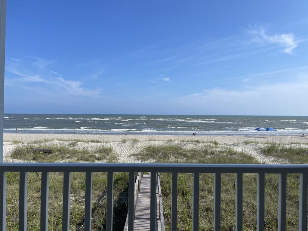 A photo of the Atlantic Ocean from the beach house I’m staying in for my vacation in Holden Beach, North Carolina. You can see the porch railing in the bottom of the photo, as well as the beach and the walkway leading to it. 