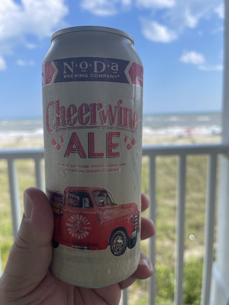 A can of Cheerwine Ale, cream with red lettering and a classic red truck, held in front of the Atlantic Ocean from our beach house deck in Holden Beach. 