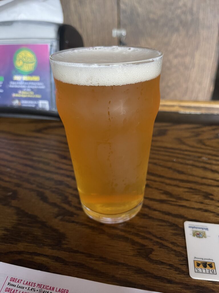 A glass of Fat Heads Juiced to Jupiter IPA. They beer is a translucent amber with a thick head of white bubbles. 