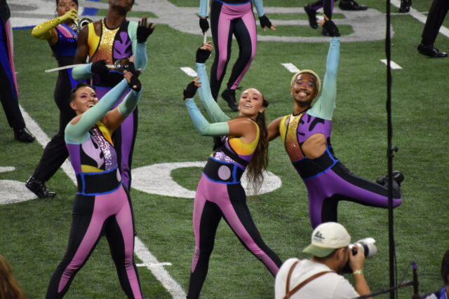 Three members of the 2023 Blue Devils Drum and Bugle Corps color guard performing during their victory encore of their program, The Cut-Outs.